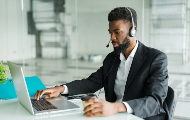 African american man customer support operator with hands-free headset working in the office. African american customer support operator with hands-free headset working in the office.
